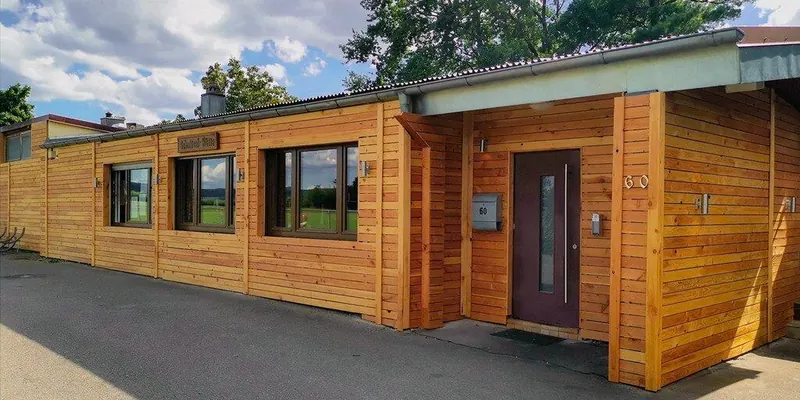 Außenansicht der Schnitzel-Hütte: langes Gebäude mit Holzfassade und Hausnummer 60