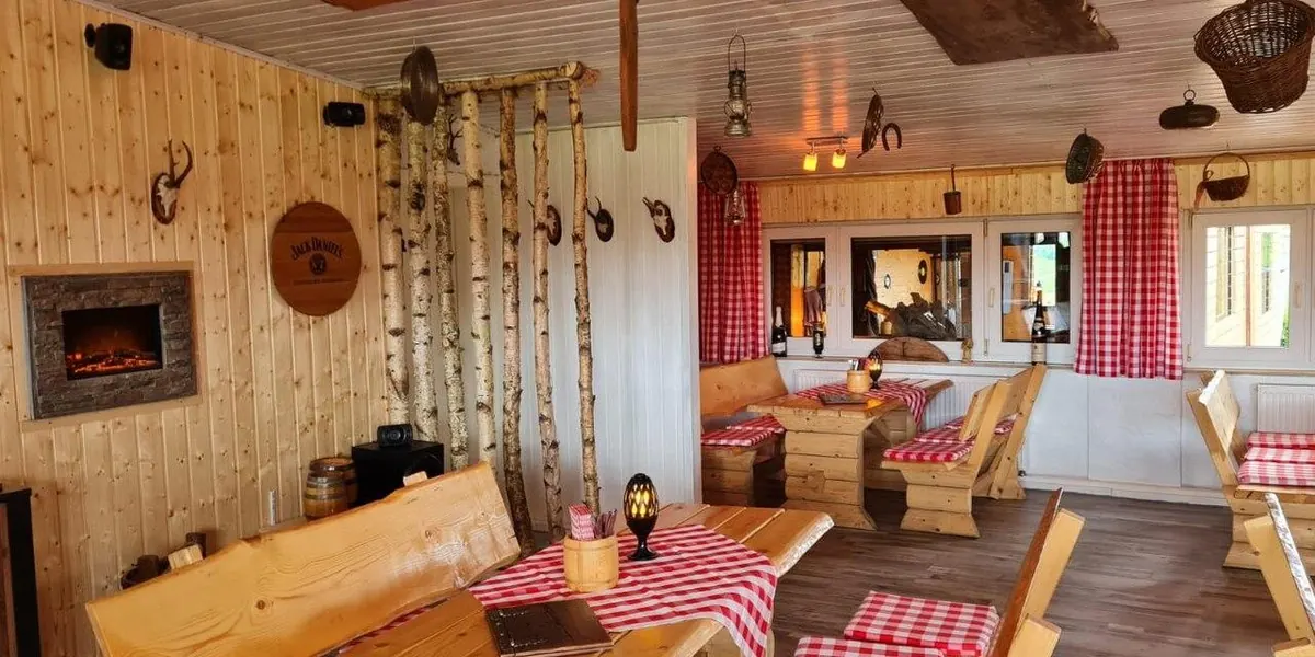 Stube der Schnitzel-Hütte mit Holzvertäfelung, Kaminofen und rot-weiß karierten Tischdecken