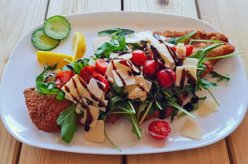 Schnitzel mit Rucola, Kirschtomaten, Parmesansplittern und Balsamicocreme auf weißem Teller